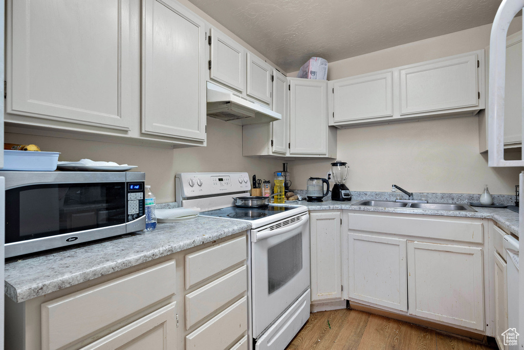 Kitchen with white electric stove, stainless steel microwave, under cabinet range hood, and light countertops