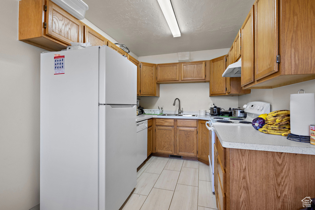 Kitchen with white appliances, under cabinet range hood, light countertops, and brown cabinetry