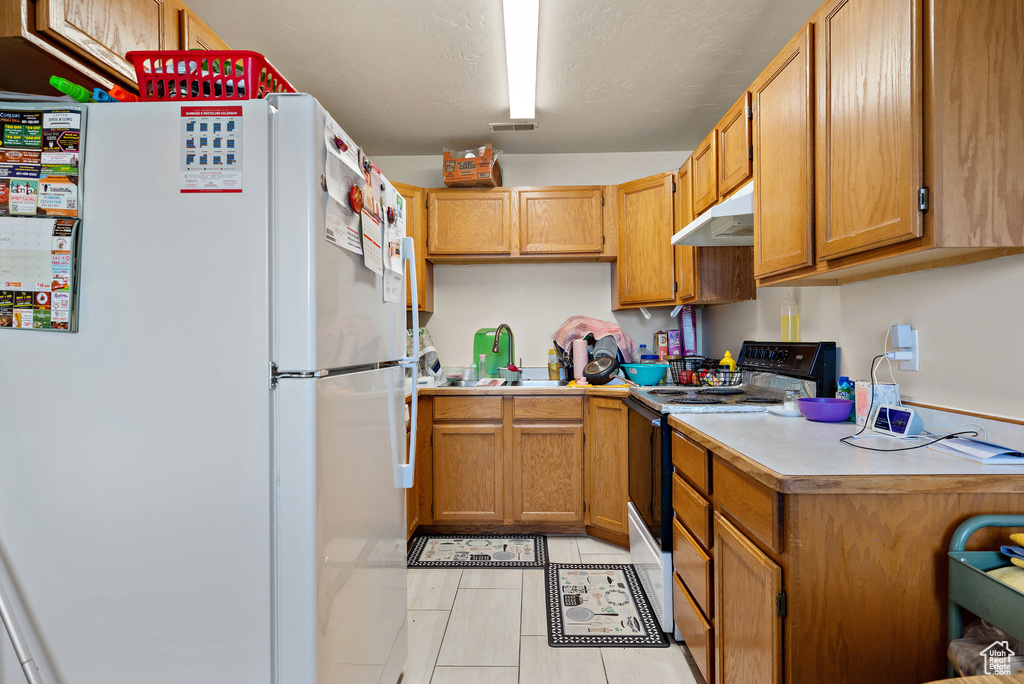 Kitchen featuring freestanding refrigerator, black electric range, under cabinet range hood, light countertops, and light tile patterned floors