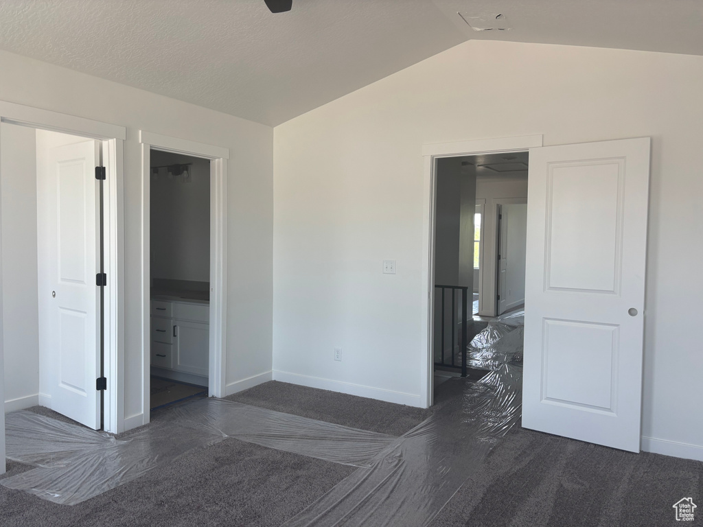 Unfurnished room featuring dark carpet and lofted ceiling