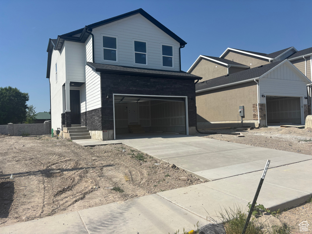 View of front of house with an attached garage, concrete driveway, and stone siding