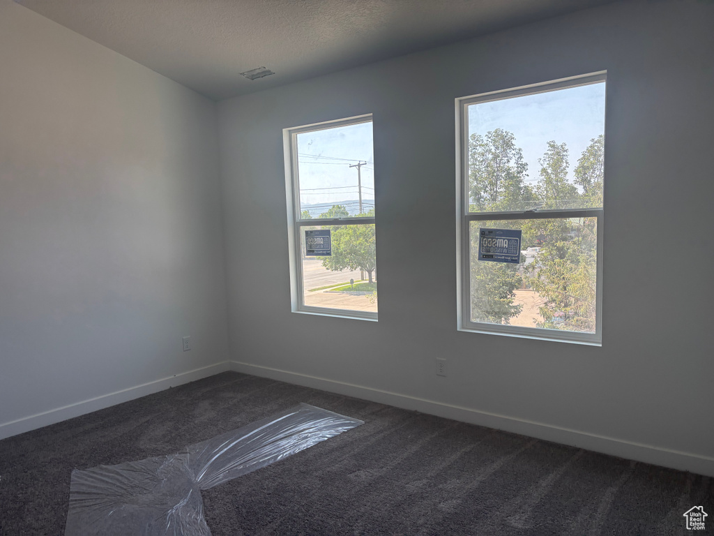 Unfurnished room featuring dark colored carpet and healthy amount of natural light