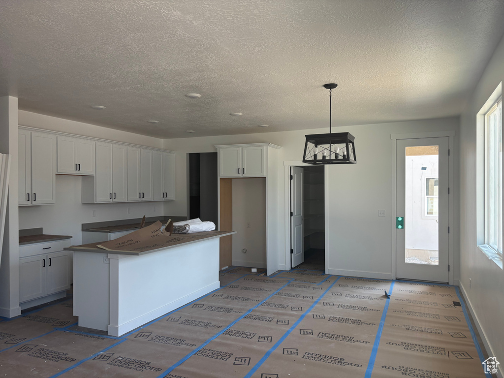 Kitchen featuring a textured ceiling, white cabinets, hanging light fixtures, and a center island