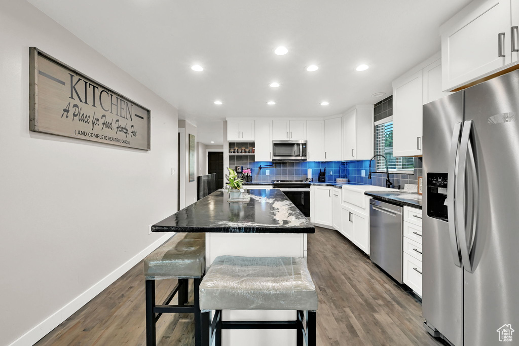 Kitchen with stainless steel appliances, decorative backsplash, dark wood-style flooring, a kitchen island, and white cabinets