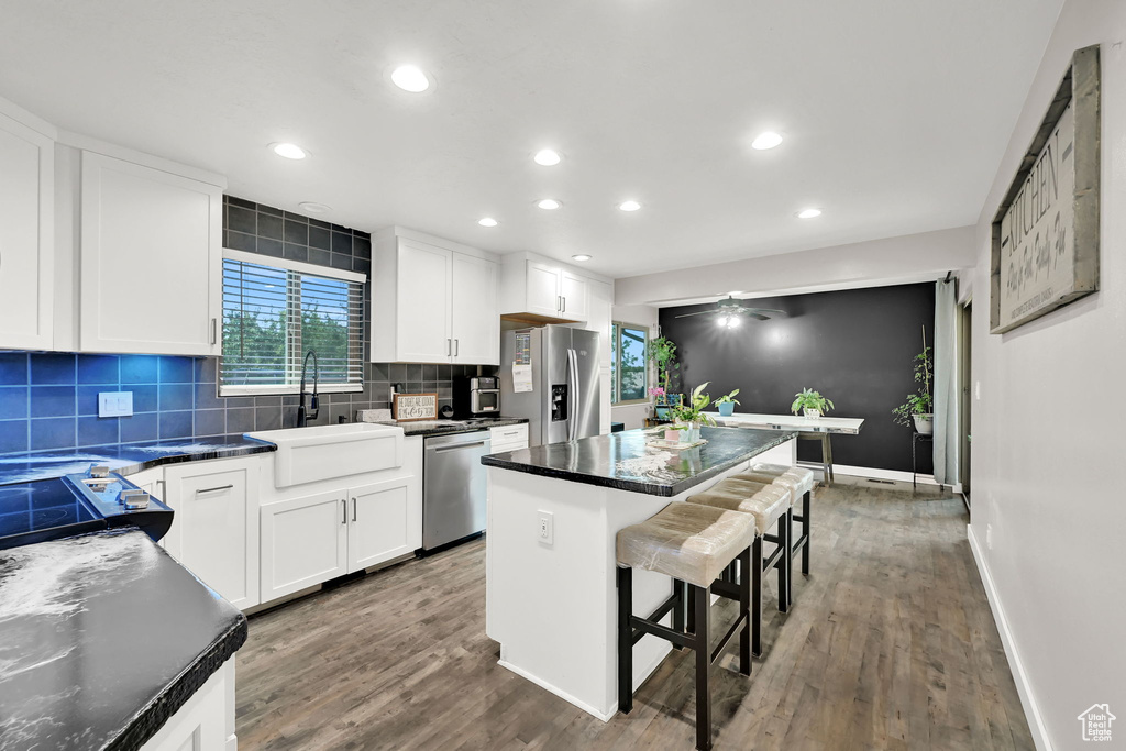 Kitchen featuring stainless steel appliances, a breakfast bar area, dark wood-type flooring, a center island, and backsplash