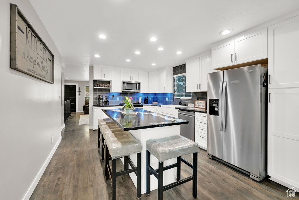 Kitchen with stainless steel appliances, dark countertops, white cabinetry, tasteful backsplash, and a kitchen island