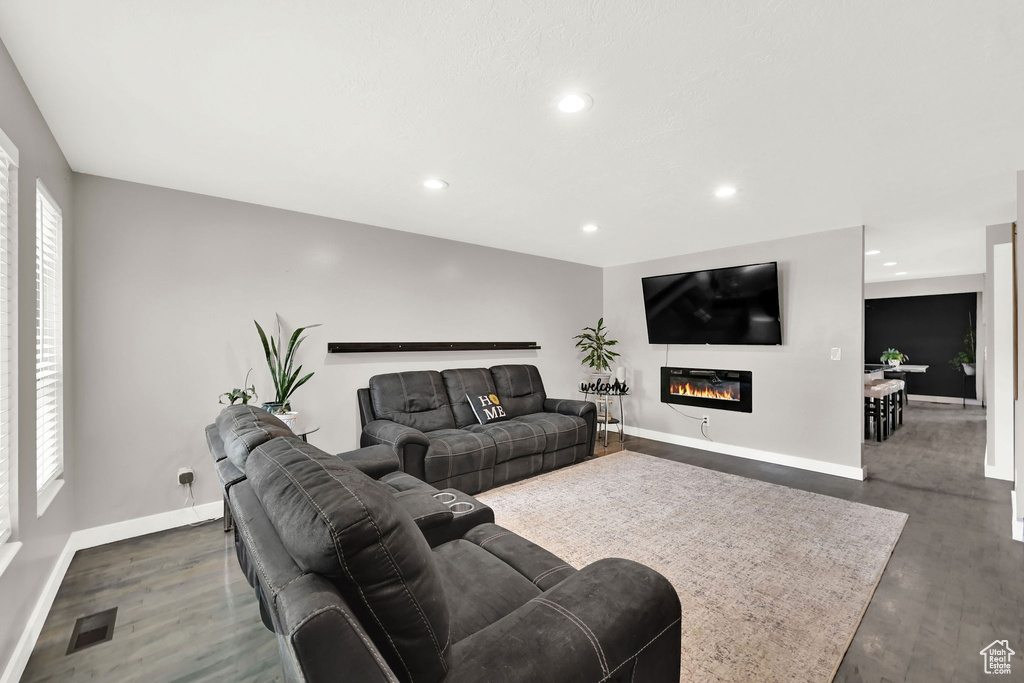 Living room with dark wood finished floors, recessed lighting, and a glass covered fireplace