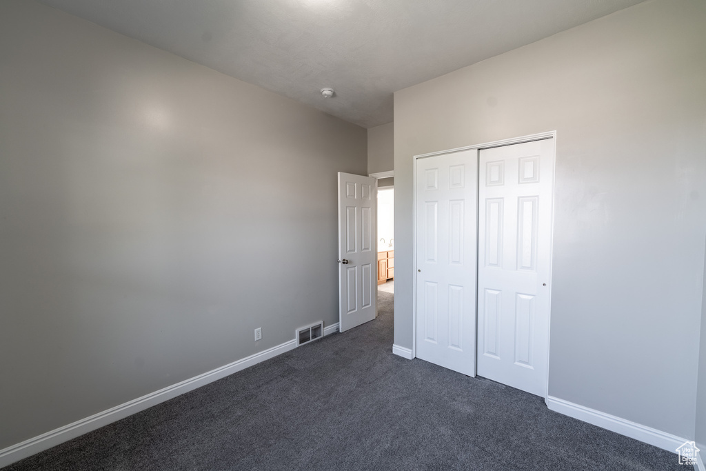 Unfurnished bedroom featuring dark colored carpet and a closet