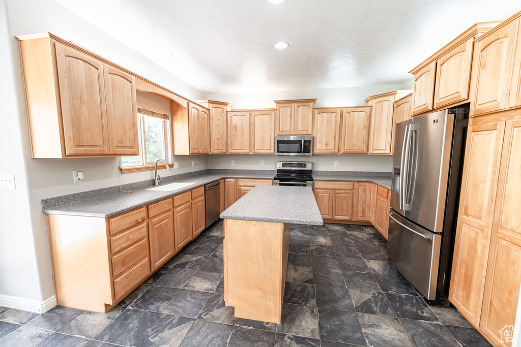 Kitchen with appliances with stainless steel finishes, light brown cabinetry, recessed lighting, a center island, and dark stone finish floors