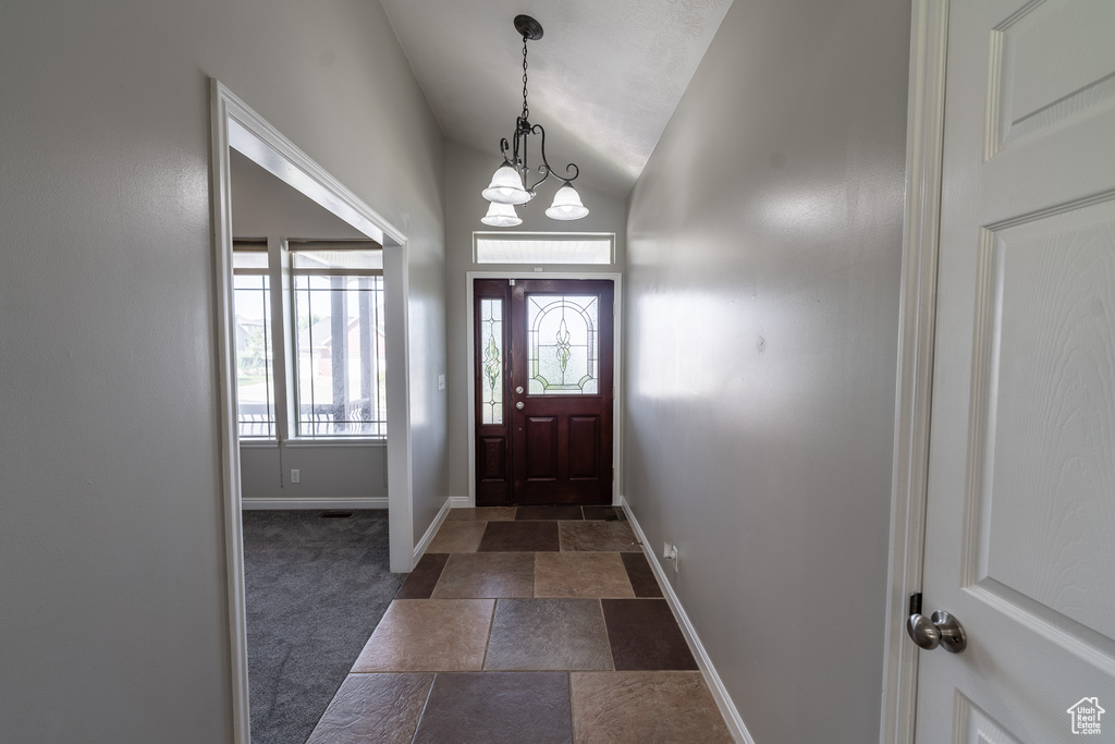 Foyer with vaulted ceiling, dark stone finish floors, and dark carpet