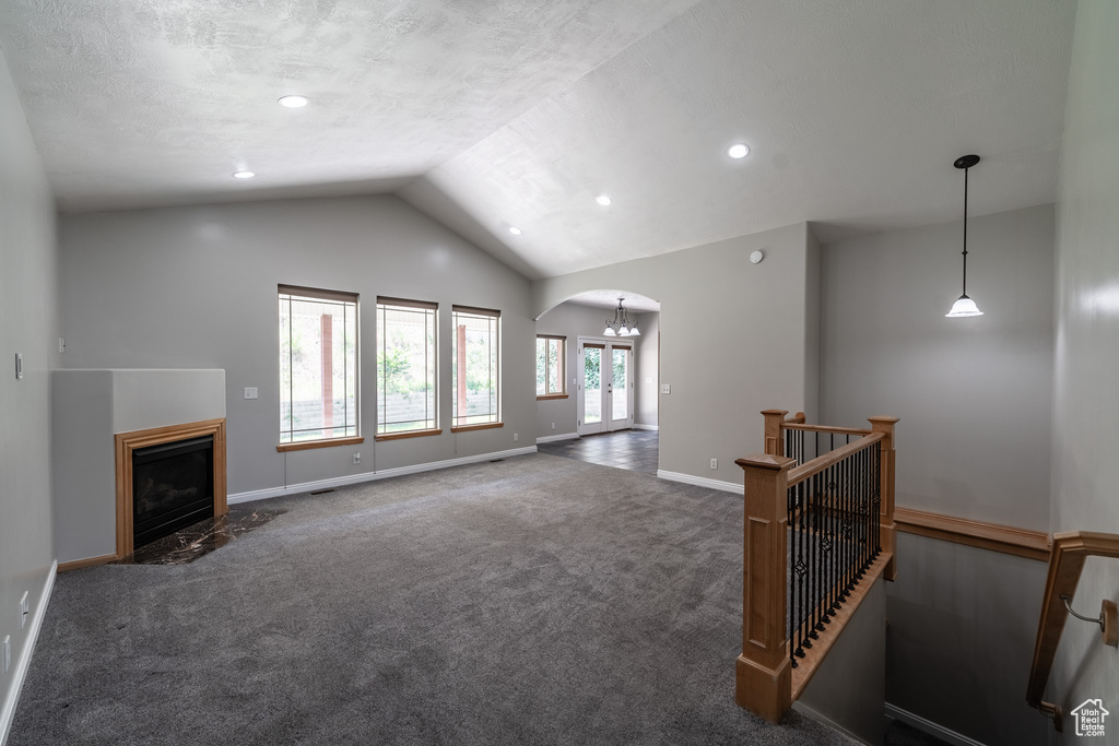 Unfurnished living room featuring arched walkways, vaulted ceiling, carpet floors, a fireplace with flush hearth, and recessed lighting
