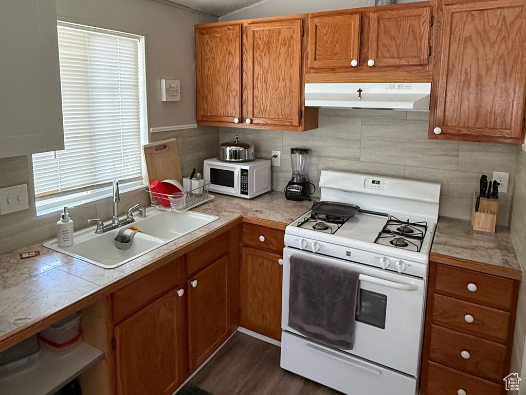 Kitchen featuring white appliances, under cabinet range hood, a textured ceiling, brown cabinetry, and dark wood finished floors