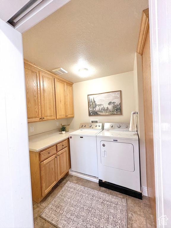 Laundry room featuring separate washer and dryer, cabinet space, a textured ceiling, and light tile patterned floors