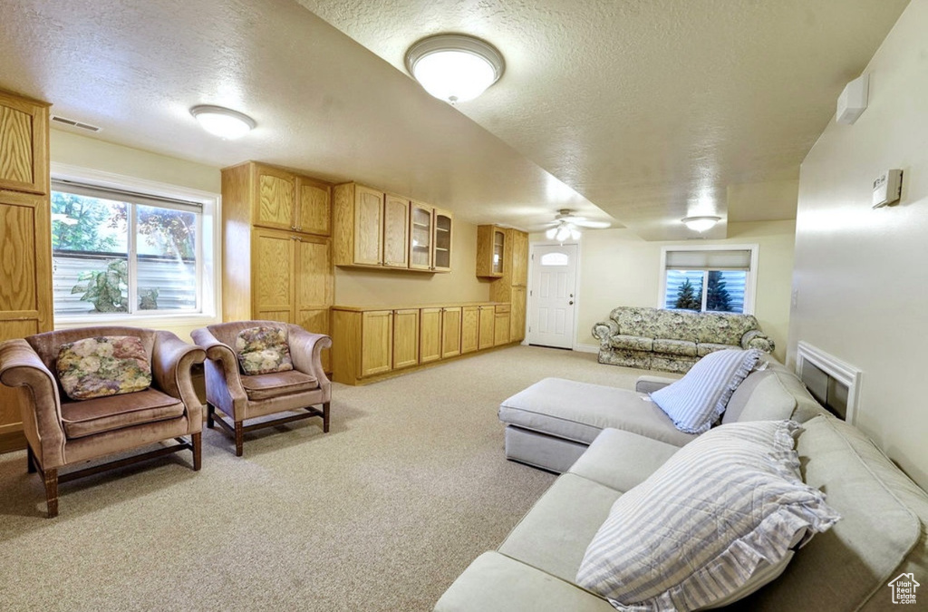 Living room featuring a textured ceiling, light carpet, healthy amount of natural light, and a ceiling fan