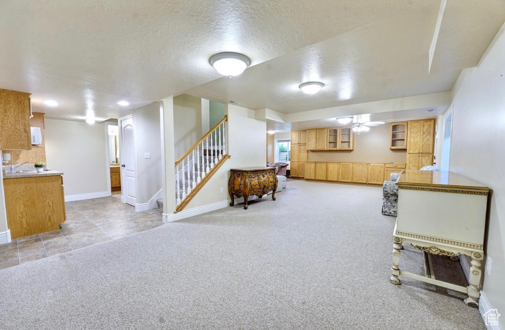 Finished below grade area with light colored carpet, a textured ceiling, stairway, and a ceiling fan