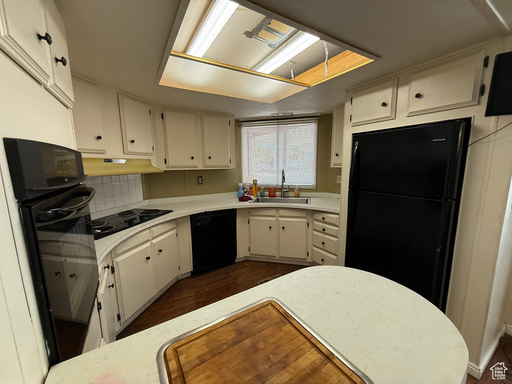 Kitchen with black appliances, light countertops, dark wood finished floors, and under cabinet range hood