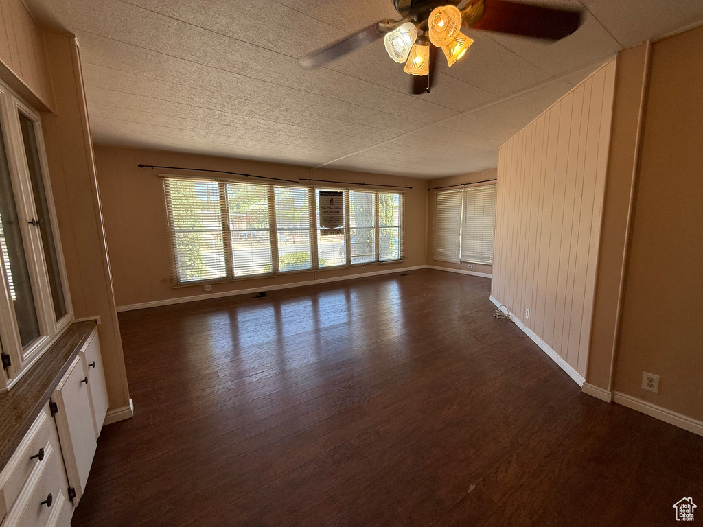 Unfurnished room with dark wood-type flooring, a ceiling fan, and healthy amount of natural light