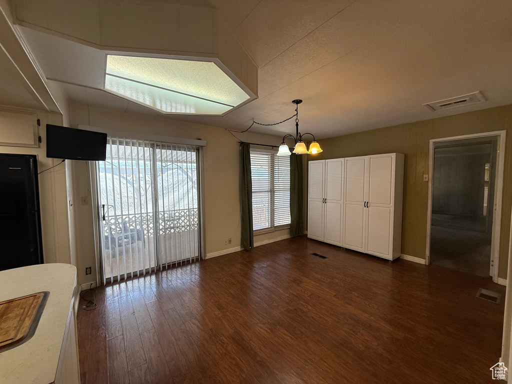 Unfurnished dining area featuring dark wood-style floors and a chandelier
