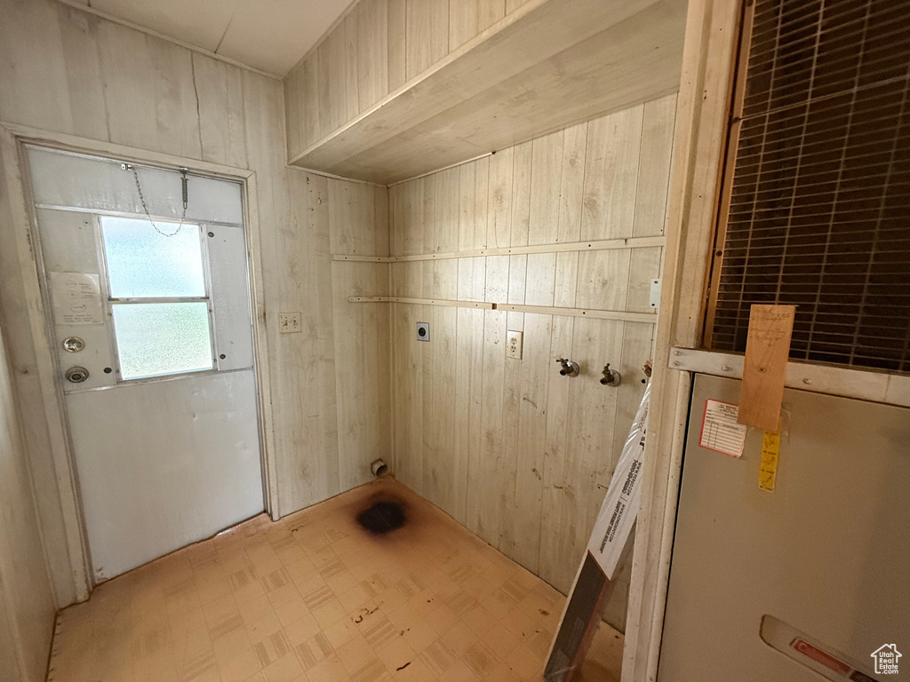 Laundry area with electric dryer hookup, wooden walls, and light floors