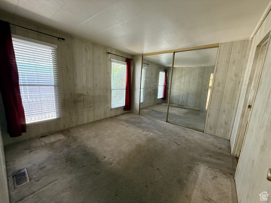 Unfurnished bedroom featuring multiple windows, wooden walls, and a closet