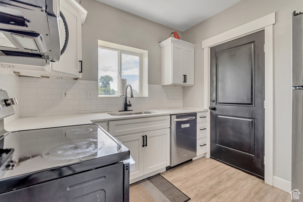 Kitchen with stainless steel dishwasher, electric stove, white microwave, tasteful backsplash, and white cabinetry