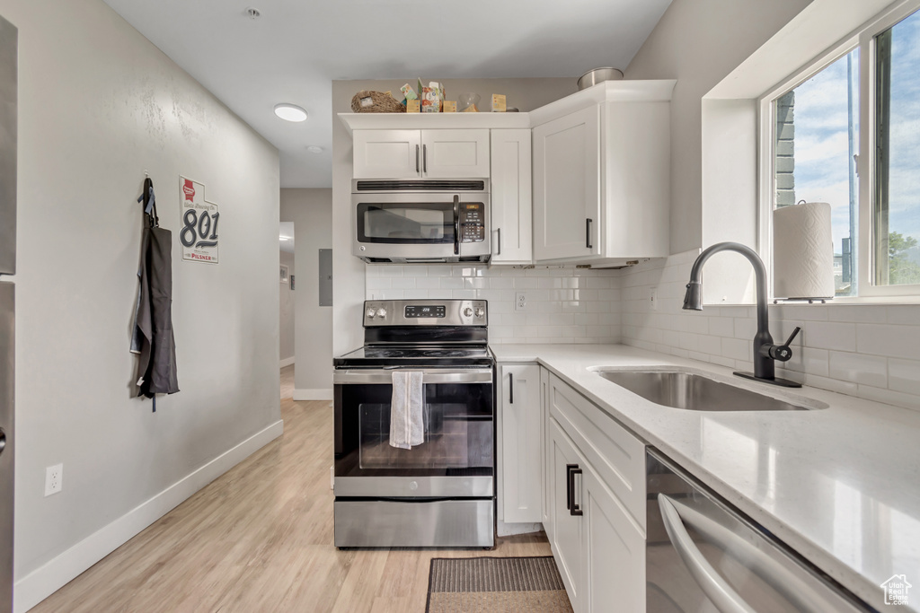 Kitchen with stainless steel appliances, backsplash, white cabinets, light wood finished floors, and light stone counters