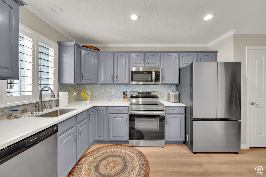 Kitchen featuring stainless steel appliances, gray cabinets, a sink, ornamental molding, and tasteful backsplash