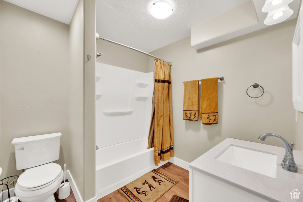 Full bathroom with vanity, toilet, wood finished floors, shower / tub combo with curtain, and baseboards