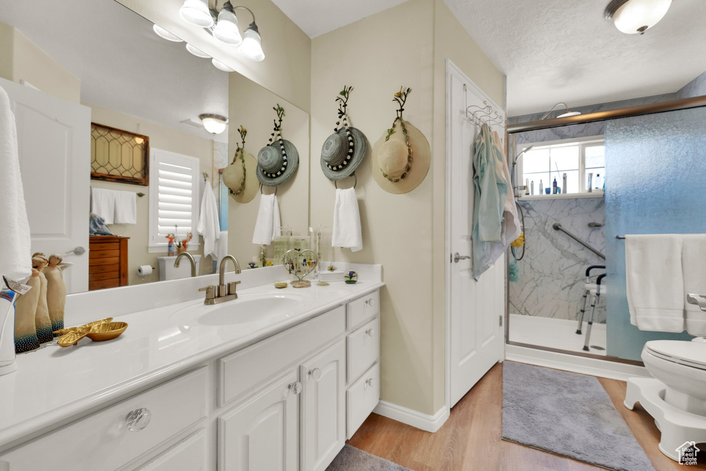 Full bath featuring toilet, vanity, a marble finish shower, wood finished floors, and baseboards
