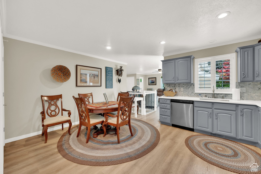 Kitchen featuring stainless steel dishwasher, gray cabinets, a sink, light wood finished floors, and backsplash