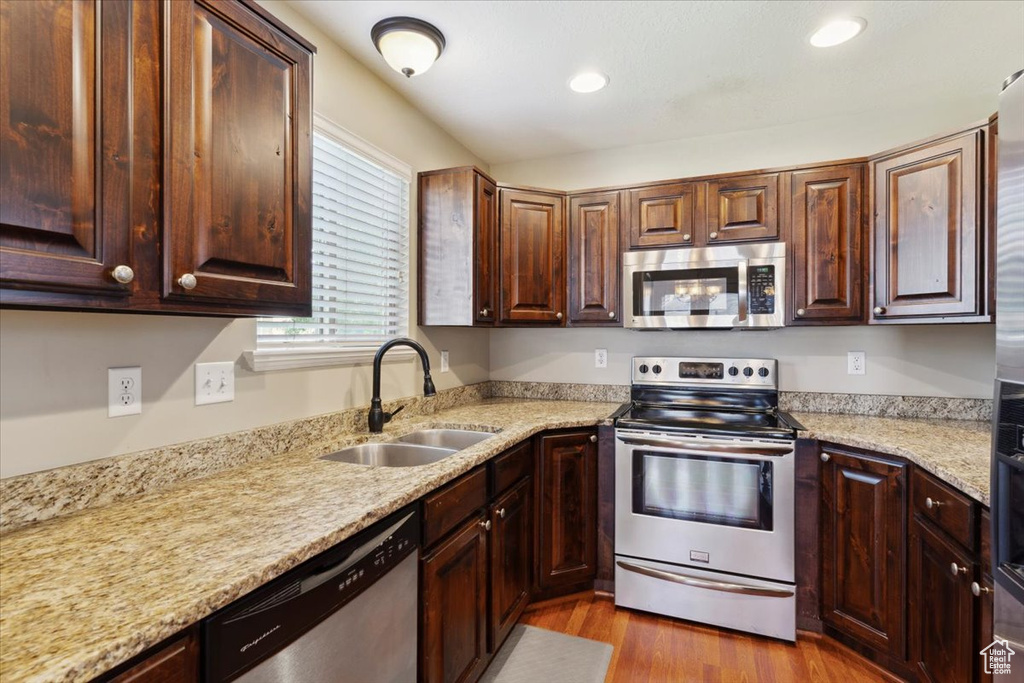 Kitchen with appliances with stainless steel finishes, wood finished floors, recessed lighting, light stone counters, and dark brown cabinets