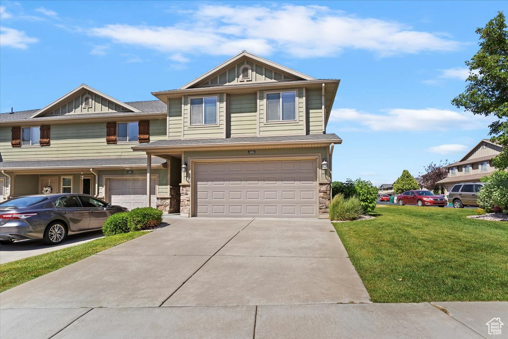 View of front facade with a garage, board and batten siding, driveway, a front yard, and stone siding