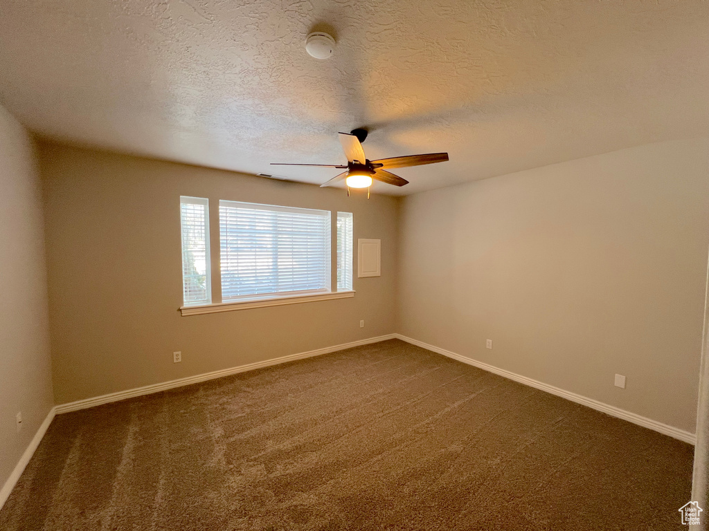 Empty room with dark colored carpet, ceiling fan, a textured ceiling, and a smoke detector
