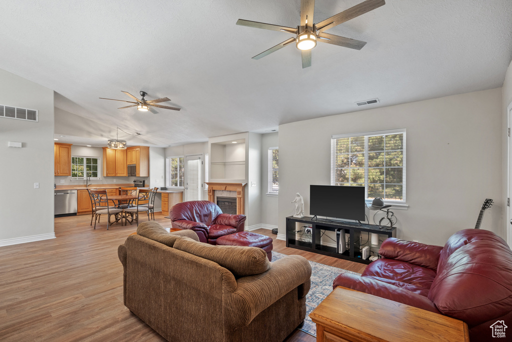 Living room with a ceiling fan, light wood finished floors, vaulted ceiling, and a fireplace