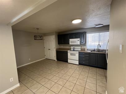Kitchen with white appliances, light tile patterned floors, light countertops, and dark cabinetry