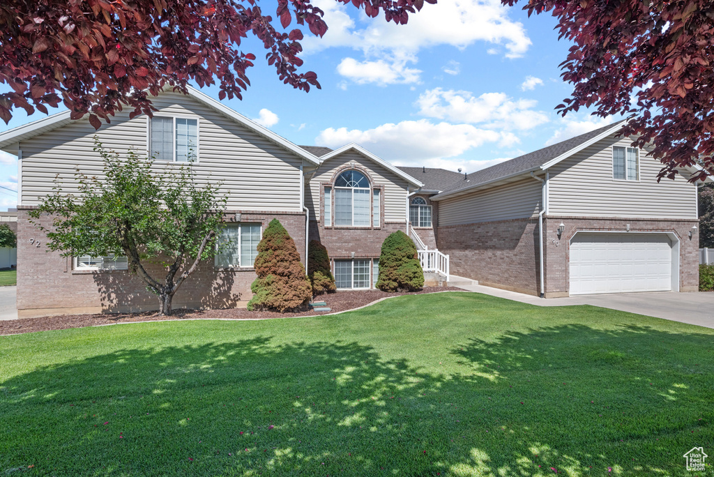 View of front of property featuring brick siding, concrete driveway, a front yard, and a garage