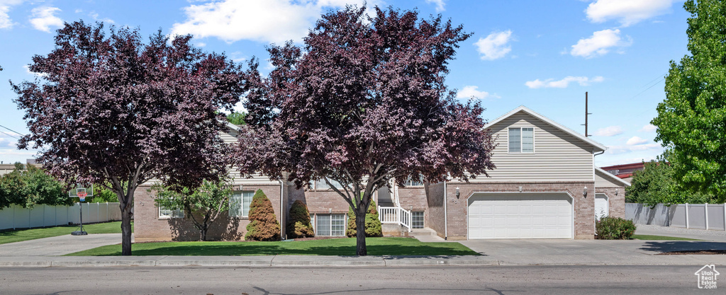View of property hidden behind natural elements with brick siding, driveway, and a garage