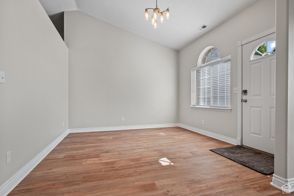Entryway with vaulted ceiling, a chandelier, and light wood-style flooring