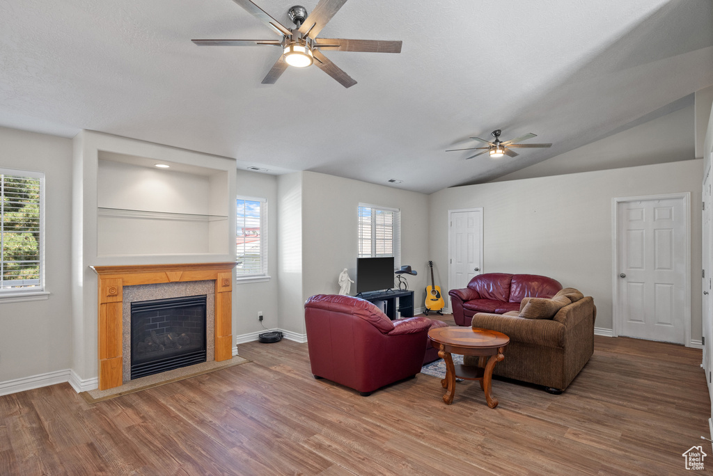 Living room featuring ceiling fan, wood finished floors, healthy amount of natural light, a tile fireplace, and vaulted ceiling