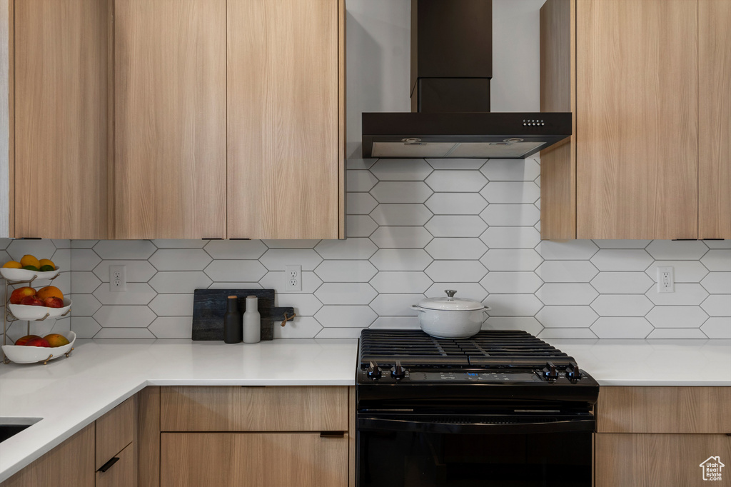 Kitchen featuring black gas range, wall chimney range hood, and modern cabinets