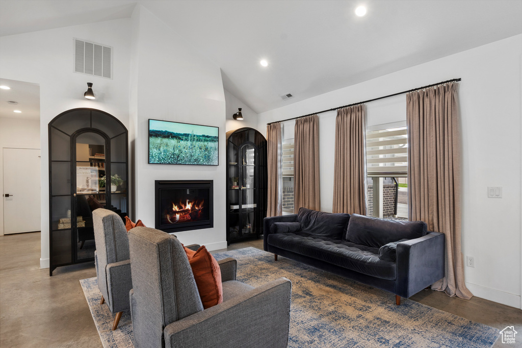 Living room featuring finished concrete floors, recessed lighting, a warm lit fireplace, high vaulted ceiling, and arched walkways