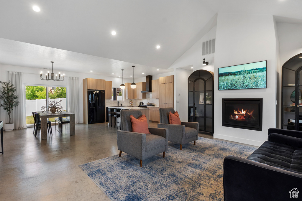 Living room with a chandelier, a glass covered fireplace, high vaulted ceiling, finished concrete flooring, and recessed lighting