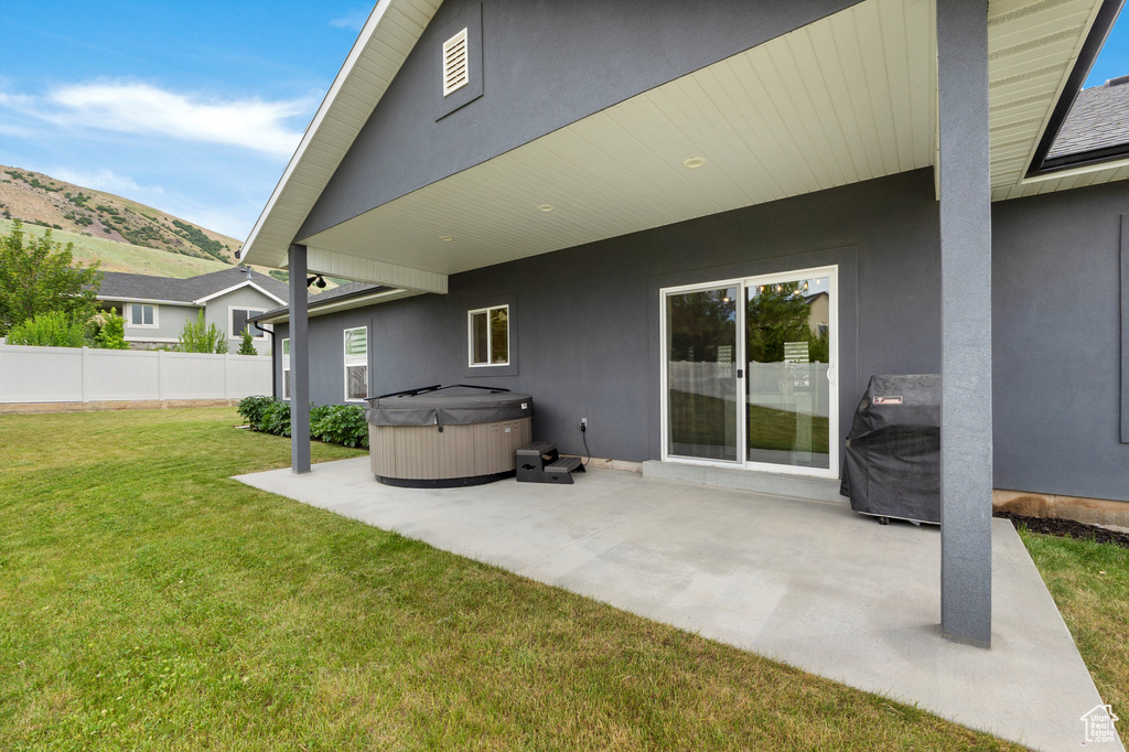 Back of property with a hot tub, a patio, stucco siding, and a mountain view