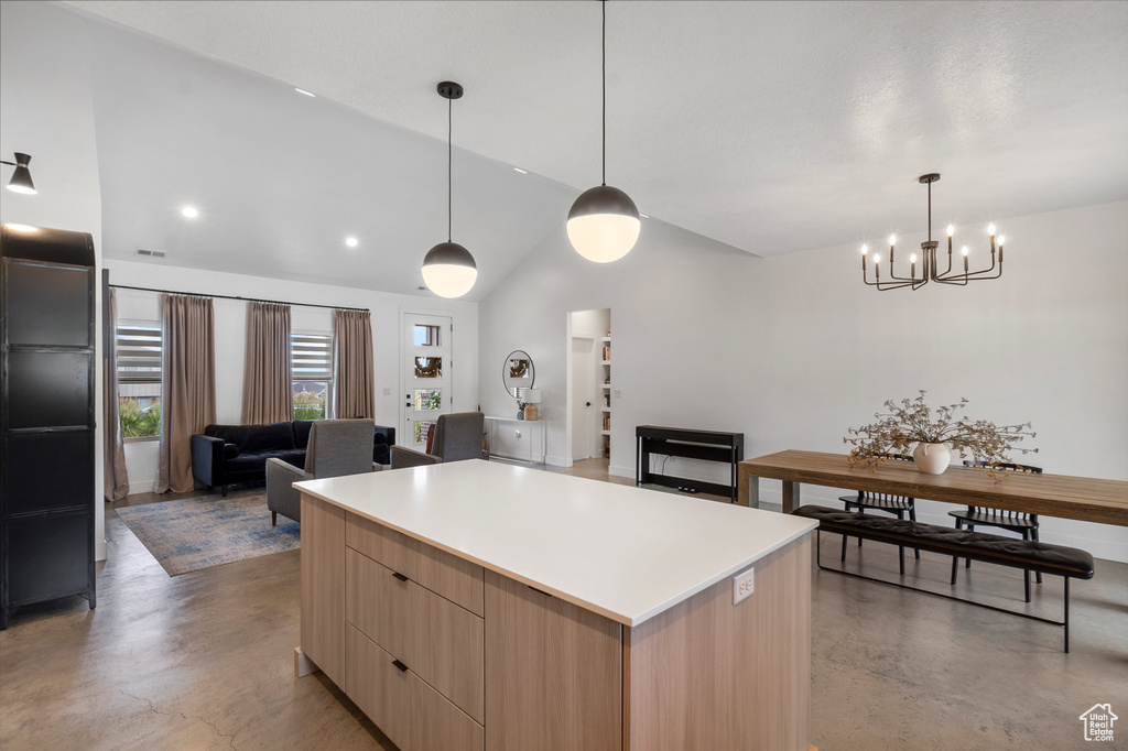 Kitchen featuring light brown cabinets, modern cabinets, finished concrete floors, lofted ceiling, and a chandelier