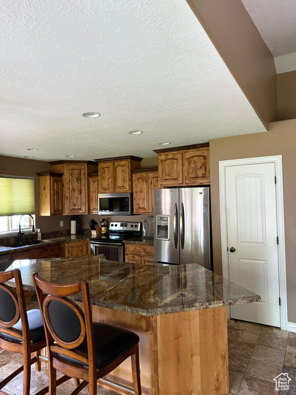 Kitchen with stainless steel appliances, brown cabinets, a breakfast bar, a center island, and recessed lighting