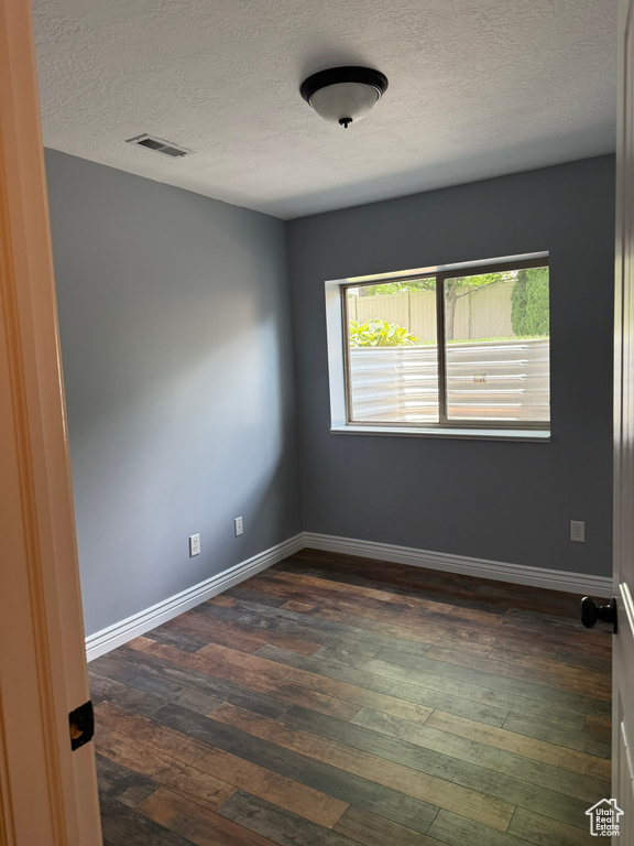 Unfurnished room with a textured ceiling and dark wood-type flooring