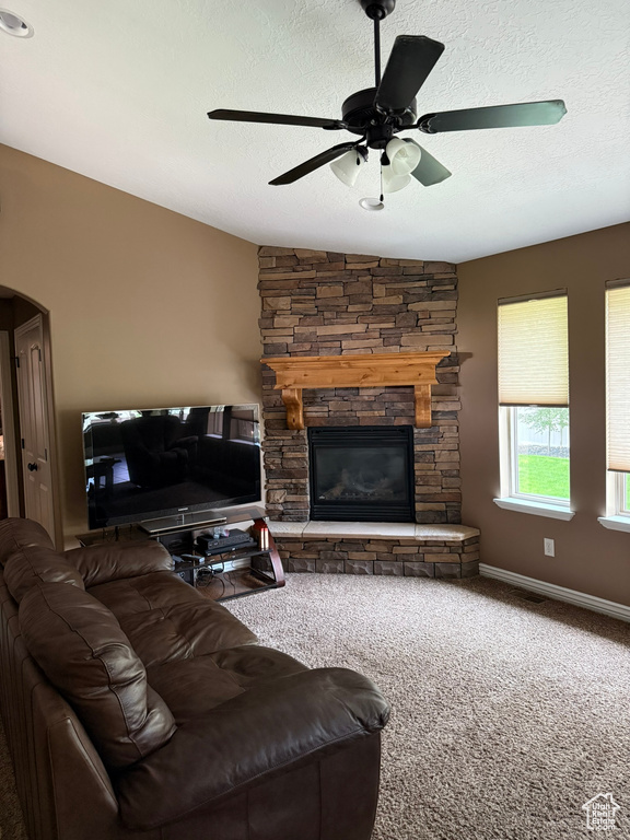 Living area featuring a fireplace, carpet, arched walkways, a ceiling fan, and a textured ceiling