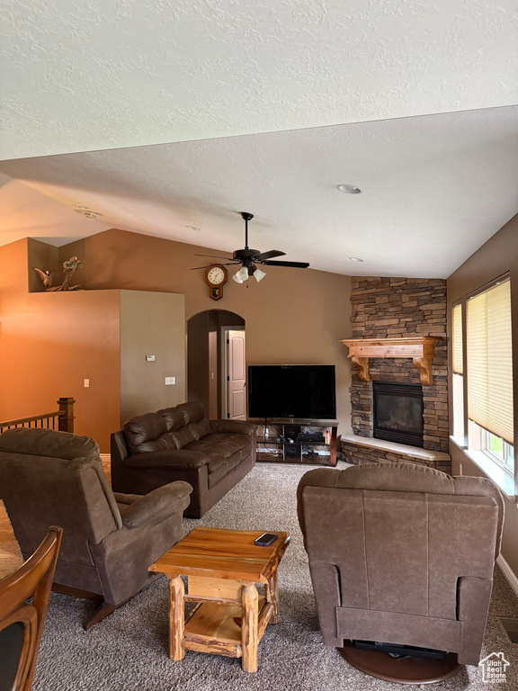 Living area with ceiling fan, a fireplace, arched walkways, lofted ceiling, and carpet