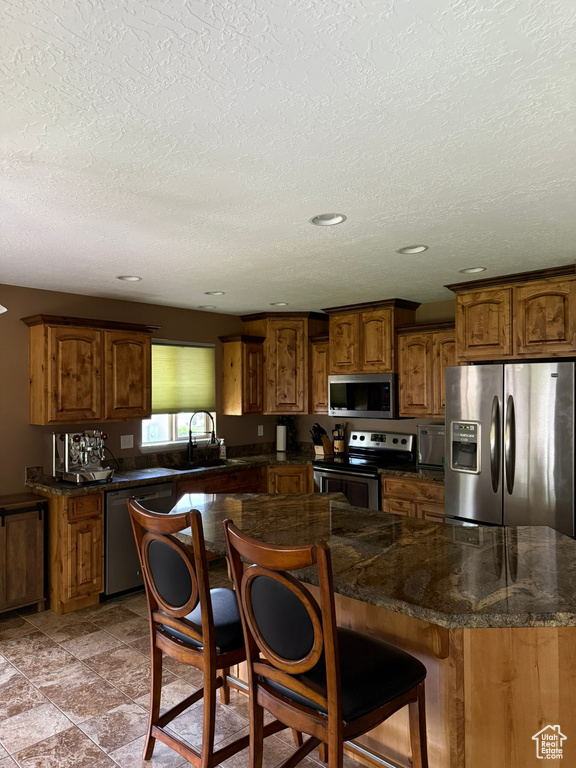 Kitchen featuring appliances with stainless steel finishes, brown cabinets, a textured ceiling, a kitchen breakfast bar, and recessed lighting