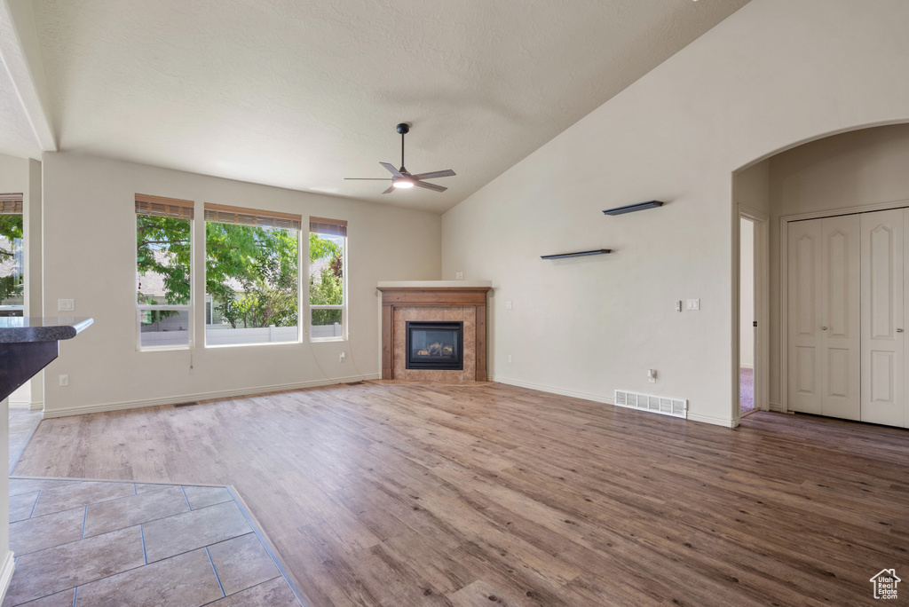 Unfurnished living room with a ceiling fan, vaulted ceiling, wood finished floors, a tile fireplace, and arched walkways